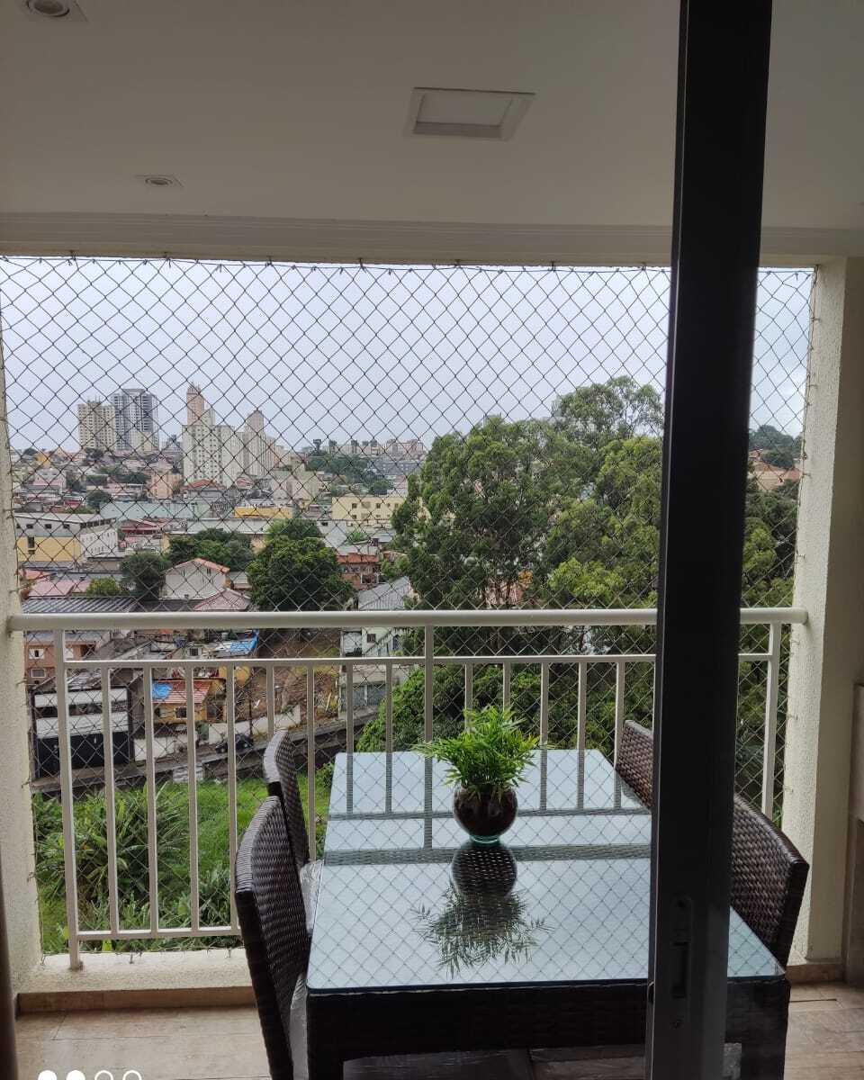 Sacada com rede de proteção, mesa de jantar e vista para a cidade